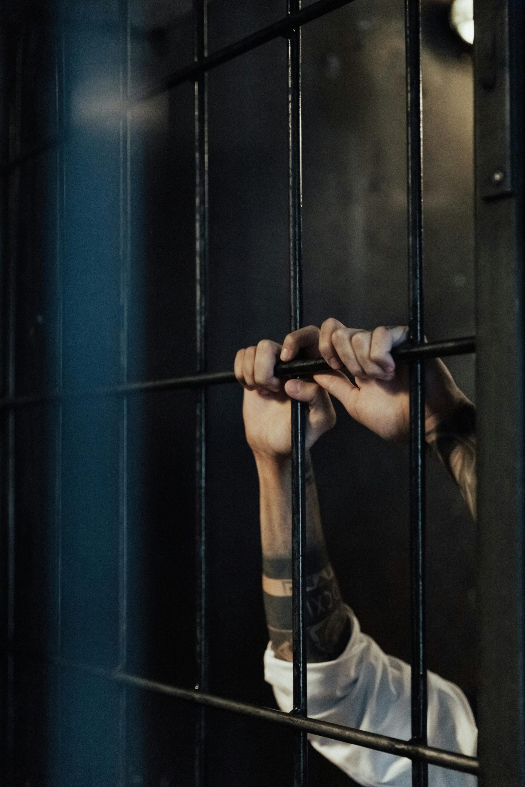 Close-up of hands holding metal prison bars, illustrating confinement and punishment.