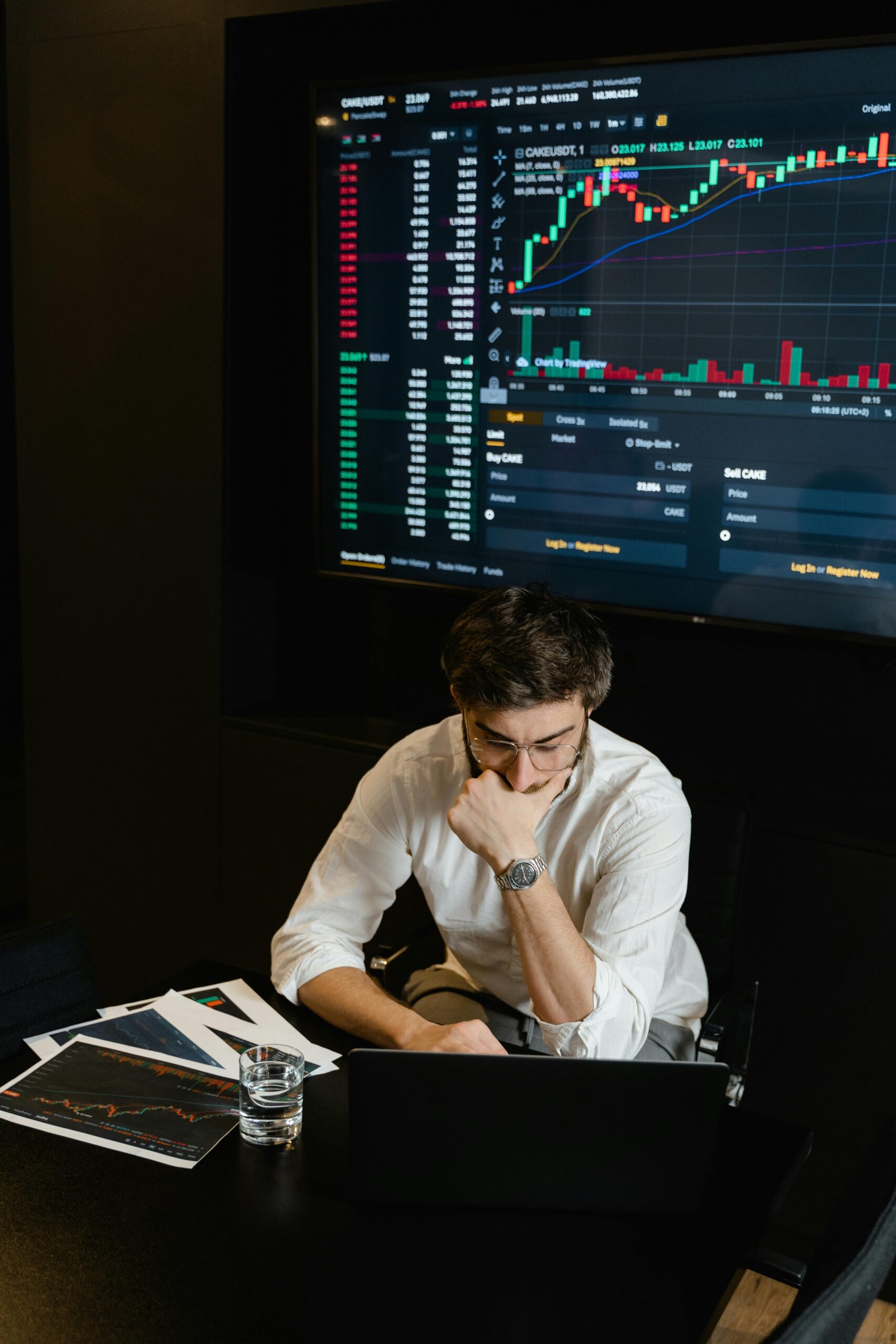 Adult man analyzing cryptocurrency data on a computer screen in an office setting.